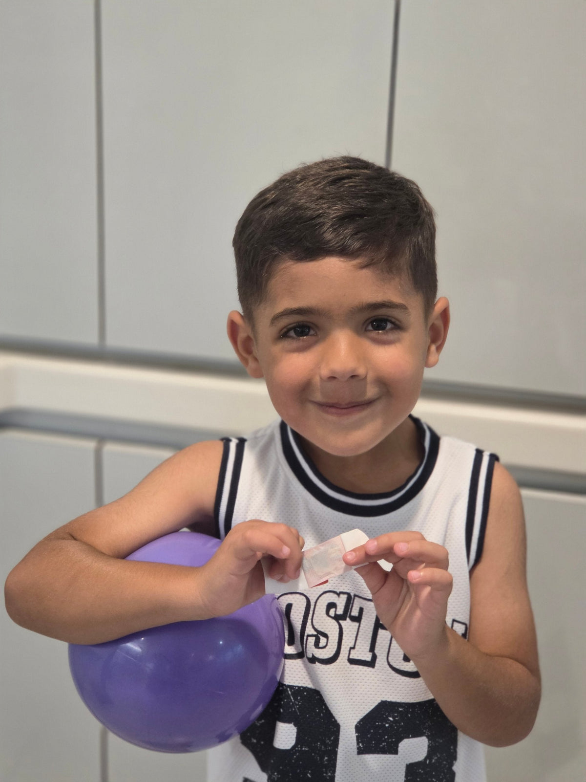 A boy in a basketball jersey holds a BooBoo Cooler® bandage close to the camera, showing the clean, dry, white cooling pouch that doesn’t drip.