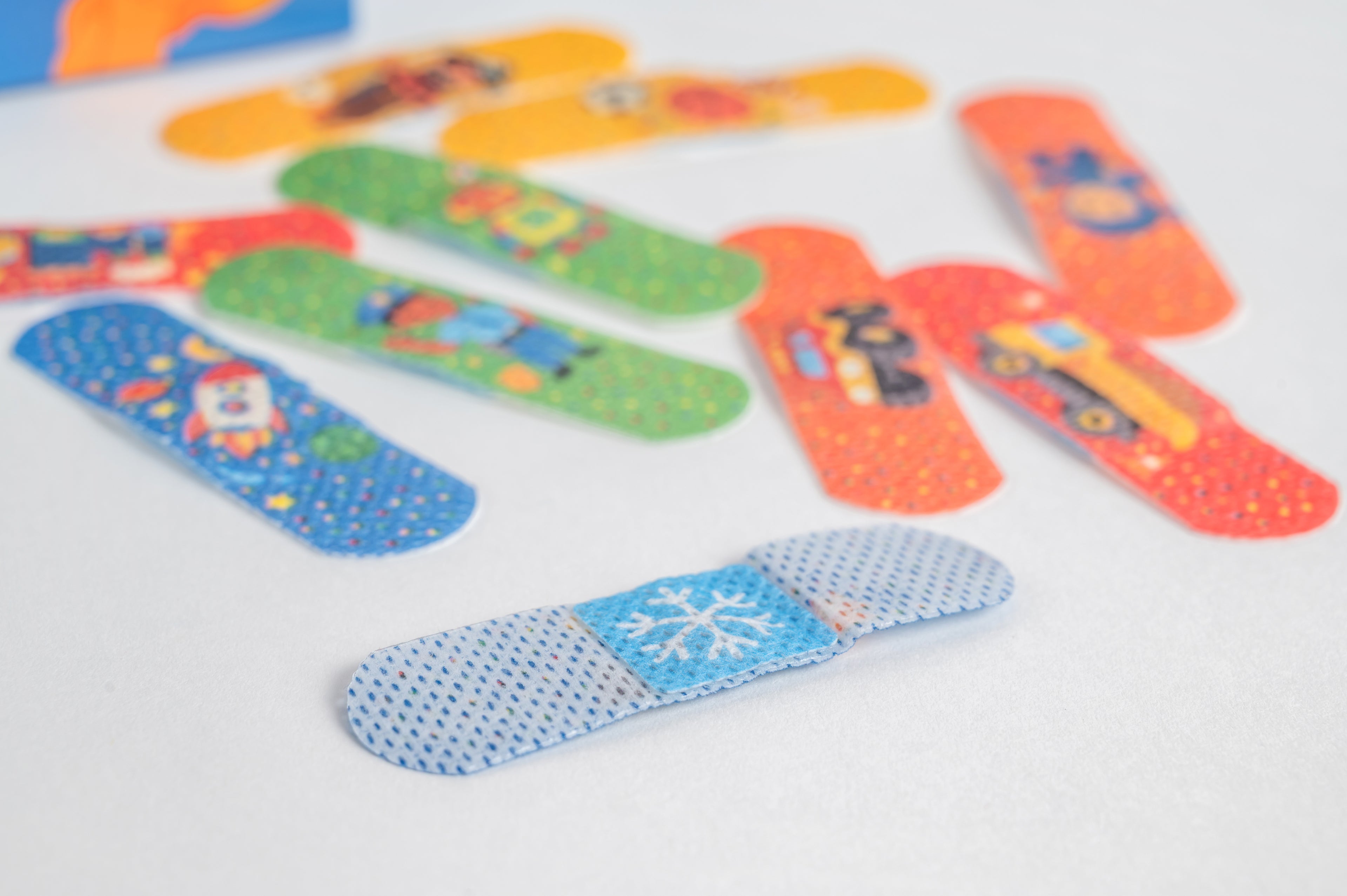 Image of BooBoo Cooler bandages with colorful desings - trucks, ninjas, rockets, sports. Also showing the skin-facing side with the snowflake cooling patch.