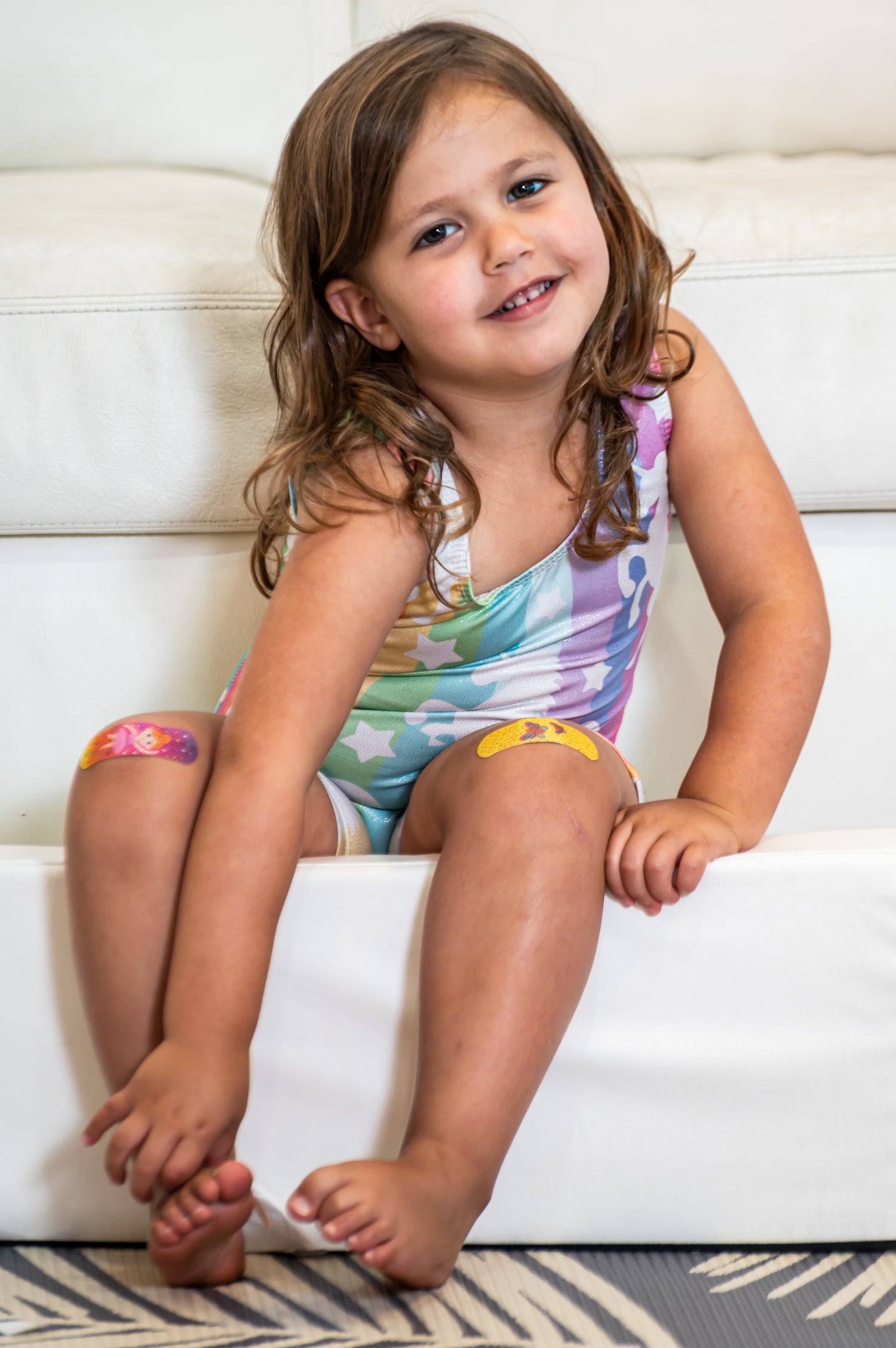 Young girl smiling in a colorful outfit with BooBoo Cooler bandages on both knees.