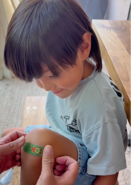 Child with a BooBoo Cooling bandage on their knee being attended to by an adult.