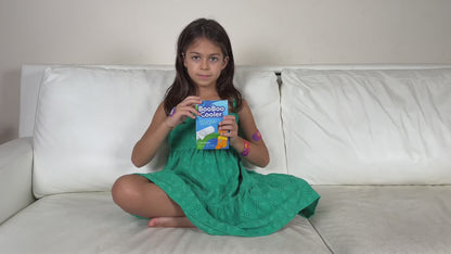 Young girl sitting on a couch in a home setting, opening a booboo cooler box to show the contents inside as she opens one of the bandages to apply on leg.