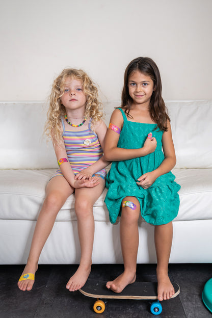 Two girls on a couch wearing BooBoo Cooler cooling bandages on arm, knee and foot
